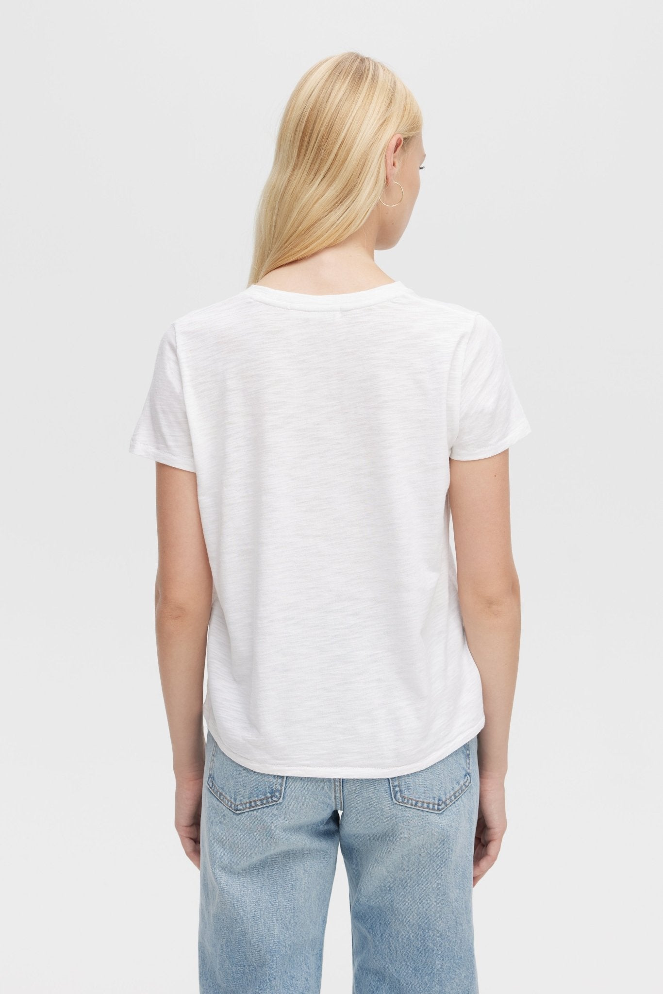 Person wearing a white t-shirt and light blue jeans on a plain background