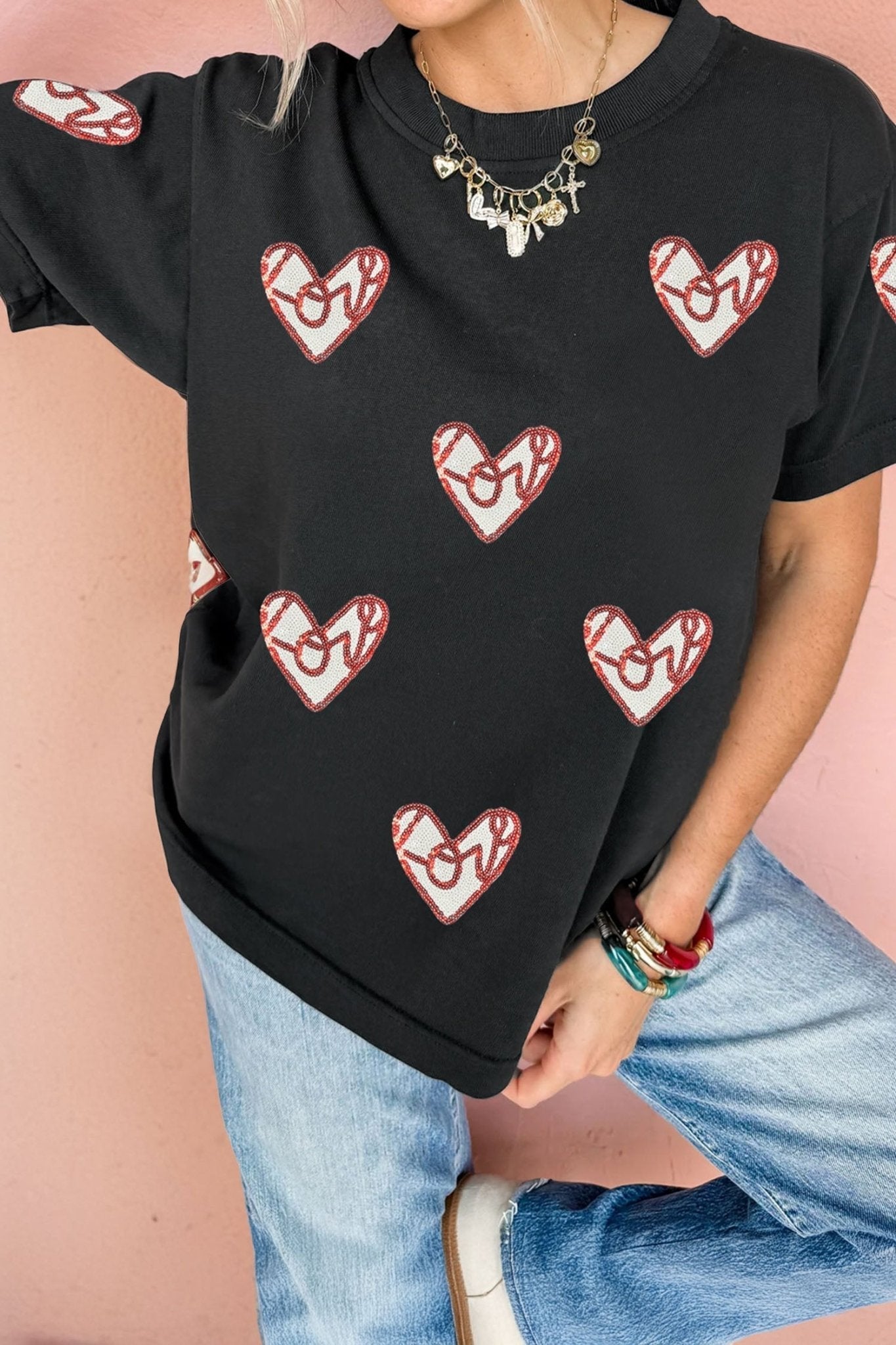 Person wearing a black t-shirt with red heart designs on a pink background