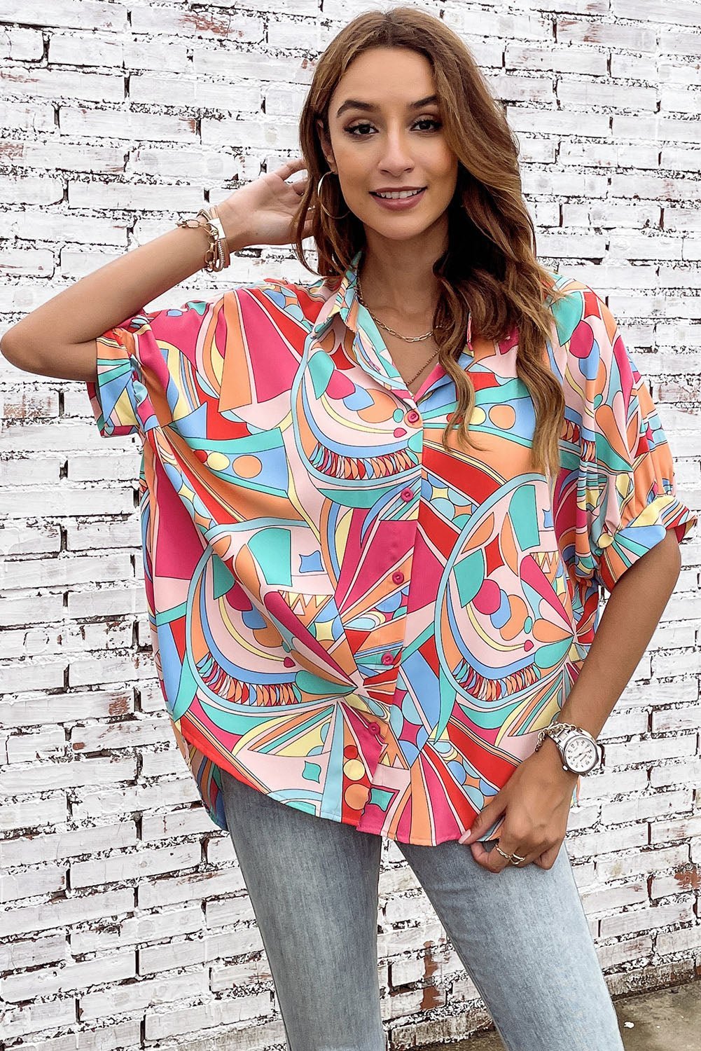 Woman wearing a colorful patterned shirt against a white brick wall.