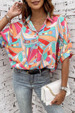 Woman wearing a colorful patterned shirt against a white brick wall.