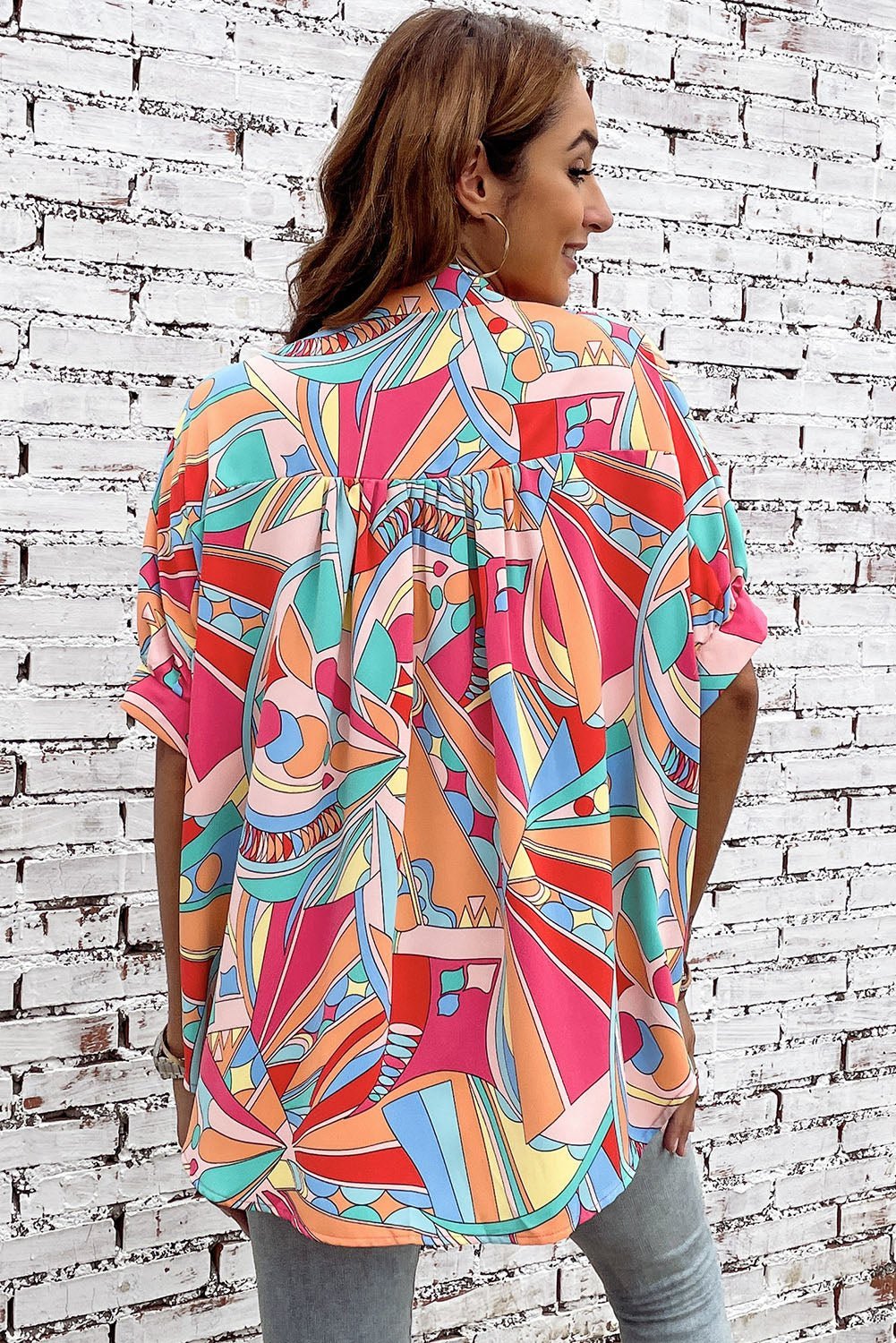 Woman wearing a colorful patterned shirt against a white brick wall.