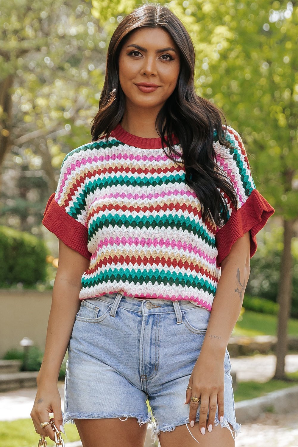 Woman wearing a colorful striped shirt and denim shorts outdoors.