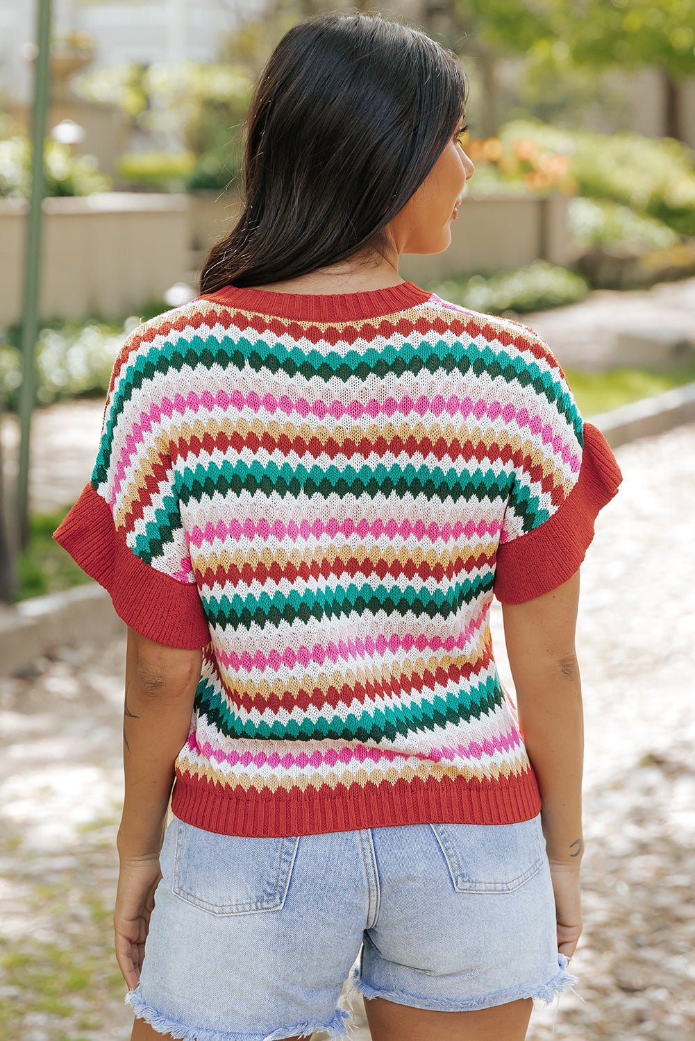 Person wearing a colorful striped sweater and denim shorts in an outdoor setting