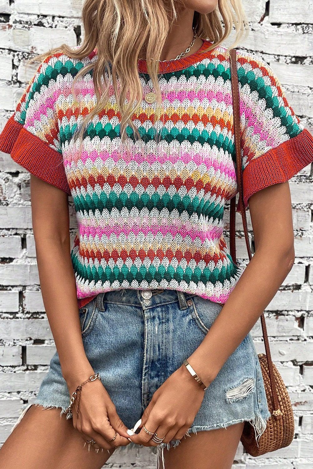 Person wearing a colorful striped sweater and denim shorts with a white brick wall background