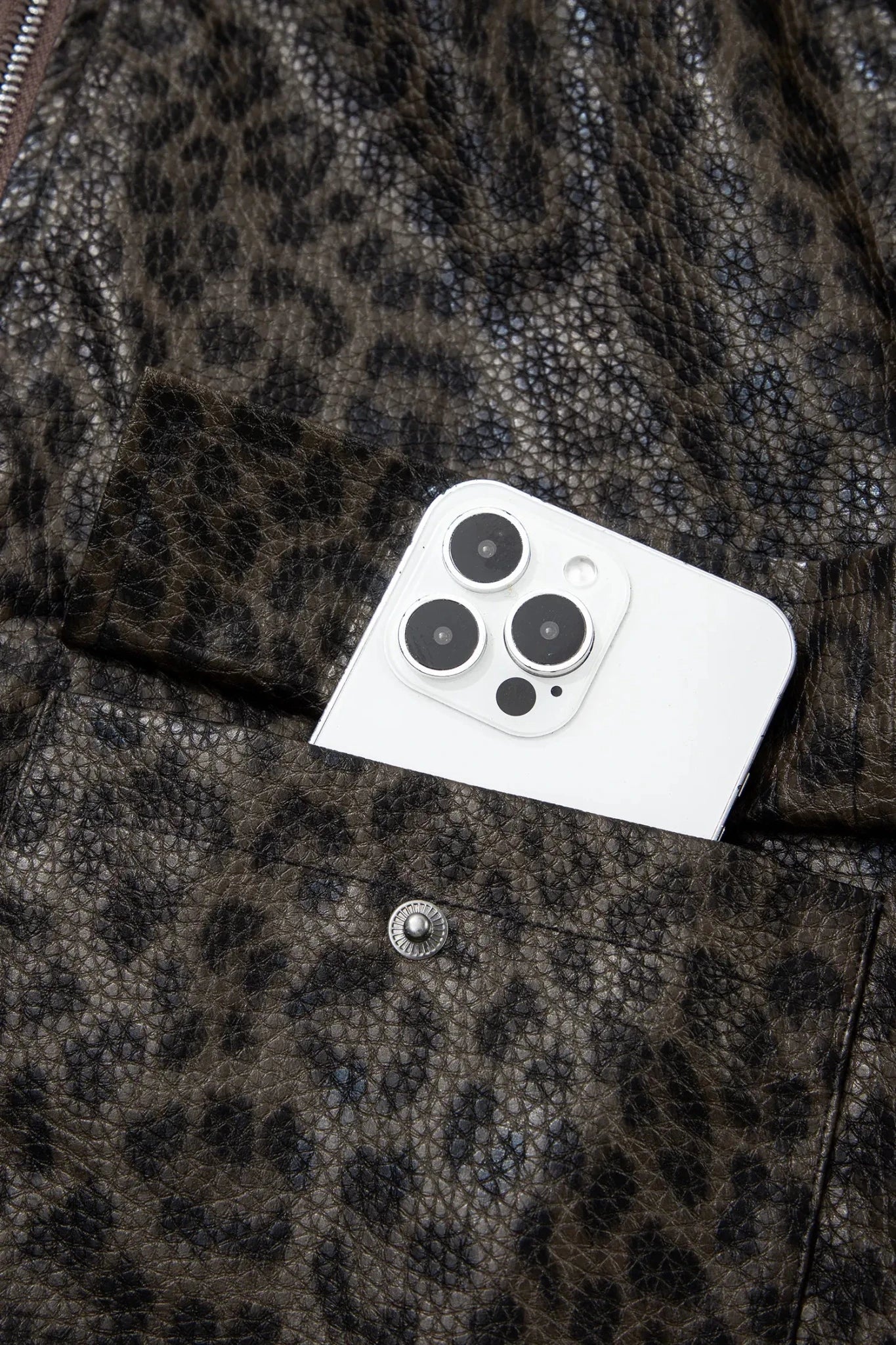 Close-up of a leopard-print faux leather jacket with a white smartphone tucked into a front pocket.