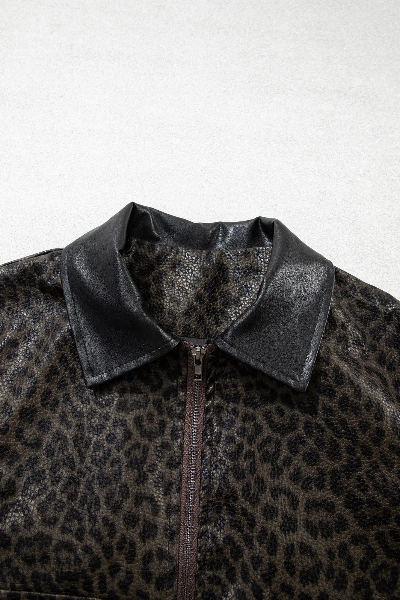 Close-up of a leopard-print jacket with a black faux-leather collar and a front zipper, shown against light gray background.