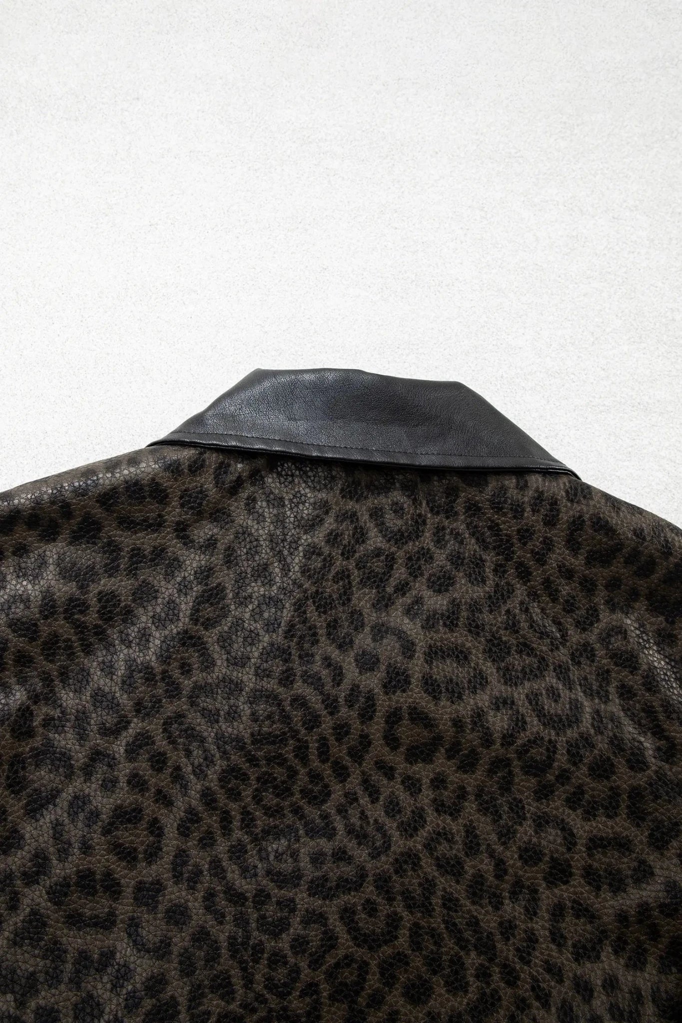 Close-up of black and brown leopard-print collar with smooth black leather-like lapel against light gray.
