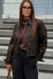 Woman in brown-black leopard jacket, dark brown top, black pants, and glasses standing on outdoor stone steps.