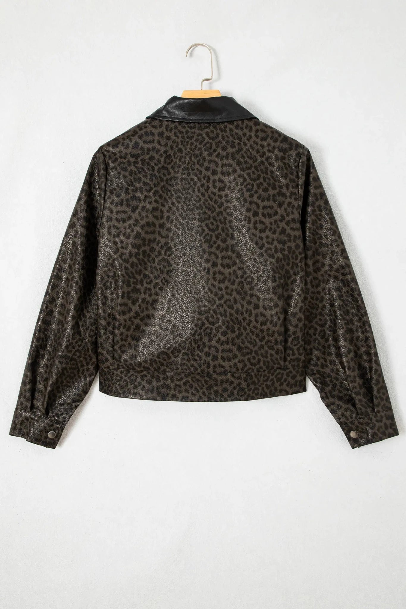 Cropped long-sleeve leopard-print jacket with contrasting black collar hanging on a wooden hanger against white.