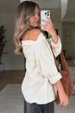Woman taking a mirror selfie wearing a white off-shoulder top and holding a brown tote bag.