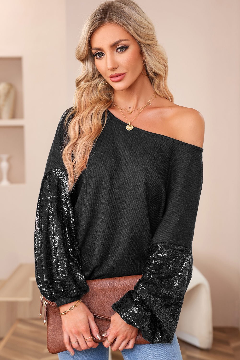 Woman wearing a black off-shoulder top with sequin sleeves, holding a brown handbag.