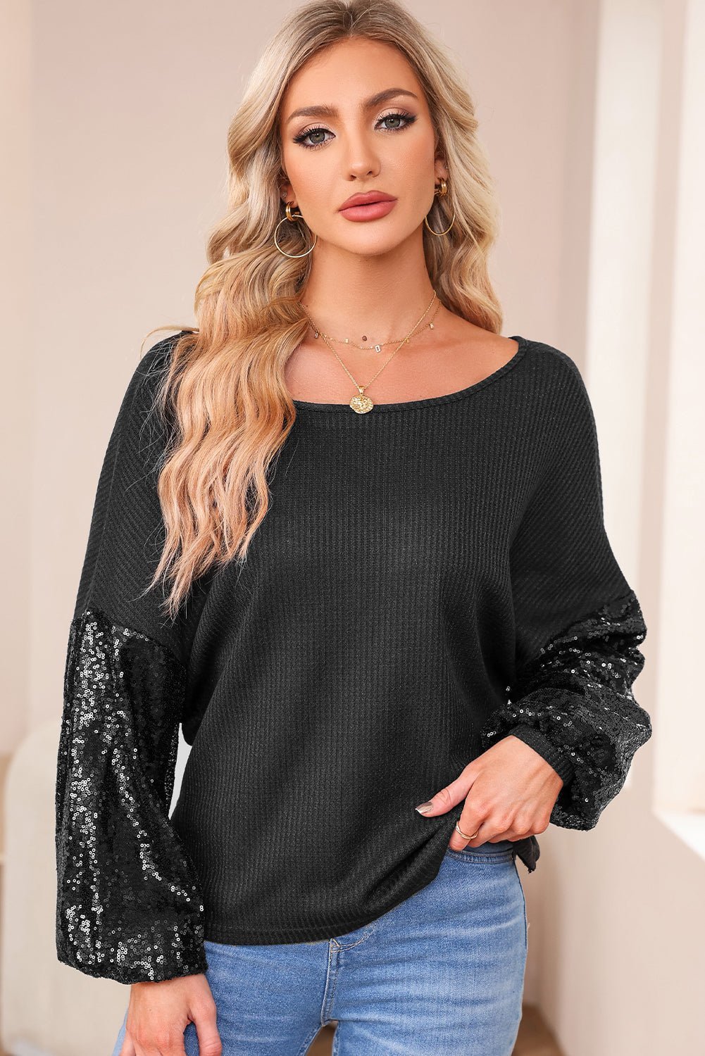 Woman wearing a black sweater with sequin sleeves against a neutral background