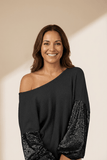 Woman wearing a black off-shoulder top with sequin sleeves on a beige background