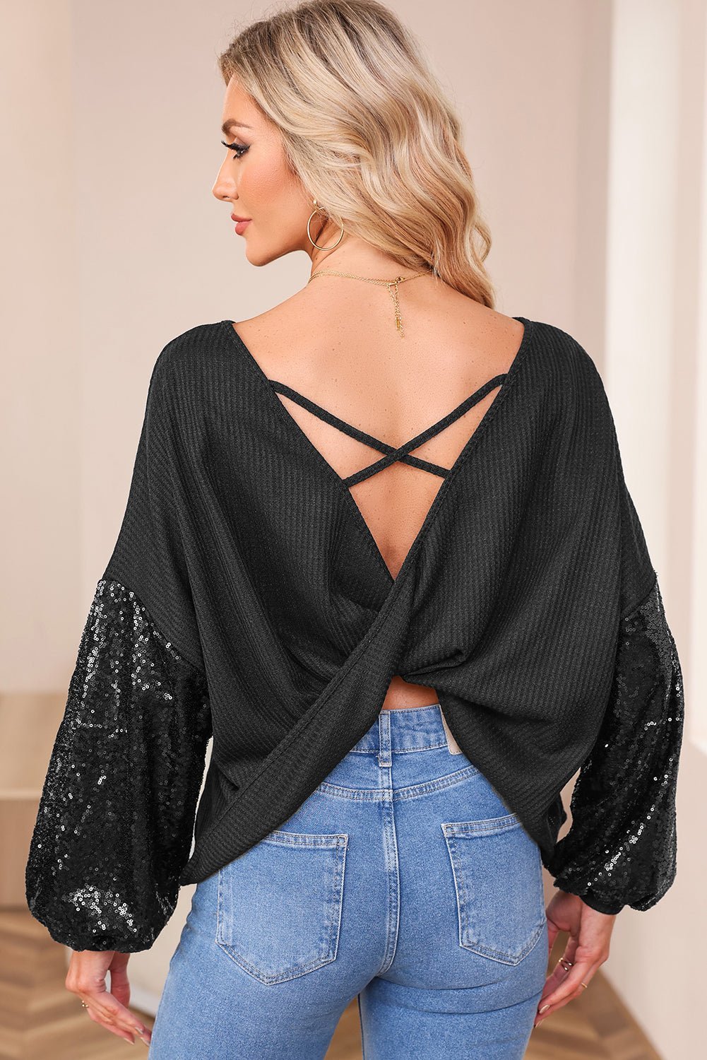 Woman wearing a black open-back top with sequin sleeves and blue jeans.
