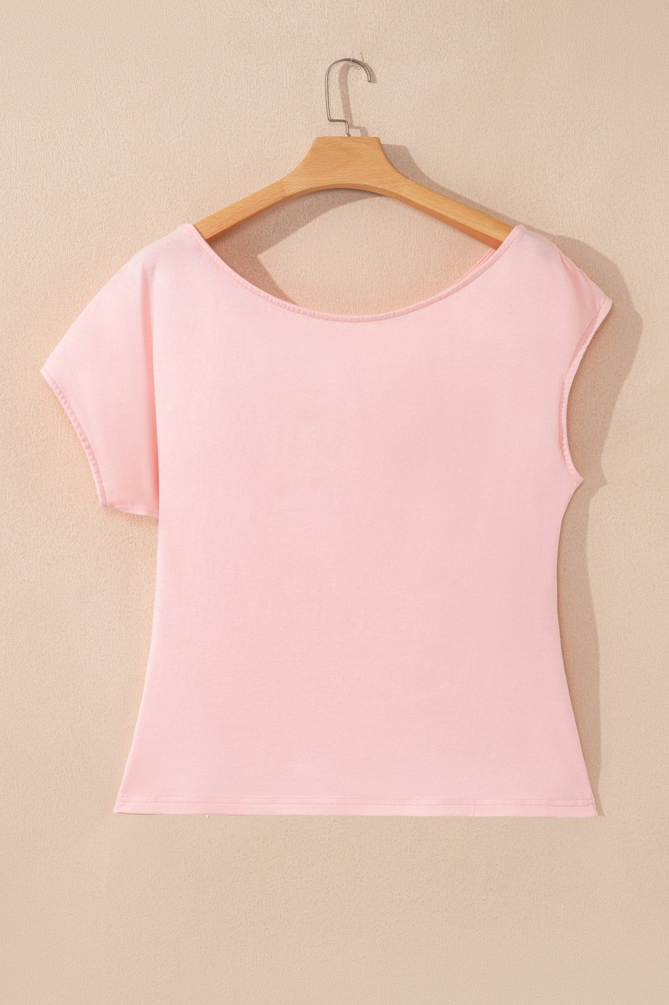 Pink sleeveless top on a wooden hanger against a beige background