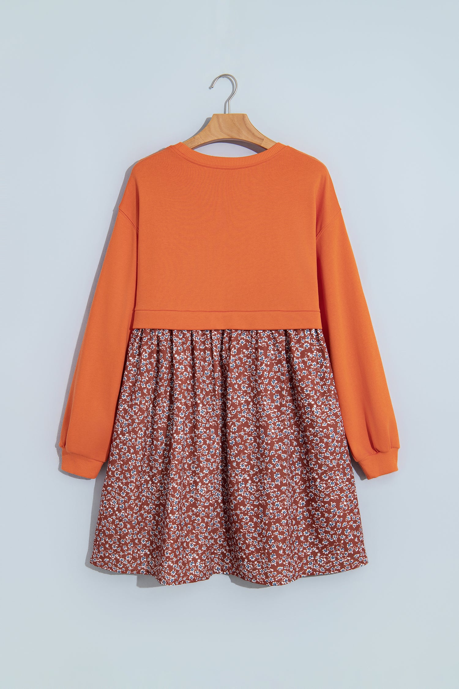 Orange and rust floral 2-in-1 long sleeve mini dress on a hanger, back view