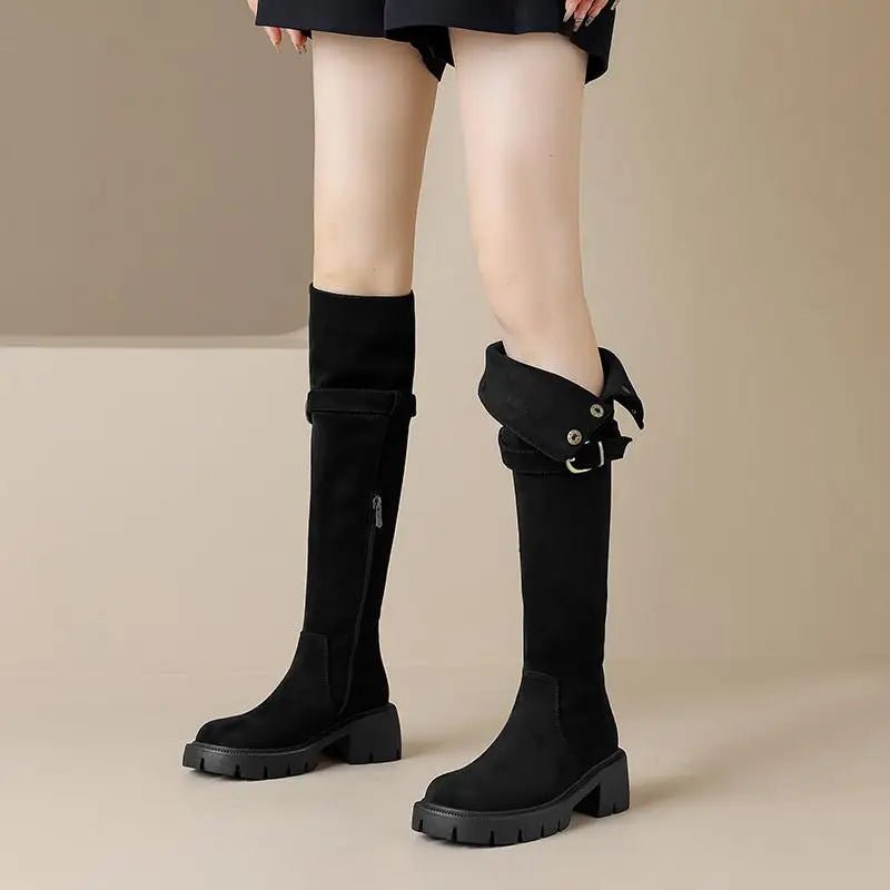 Black knee-high boots with a buckle on a beige background