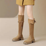 Tan knee-high boots worn with a mustard yellow skirt on a beige background