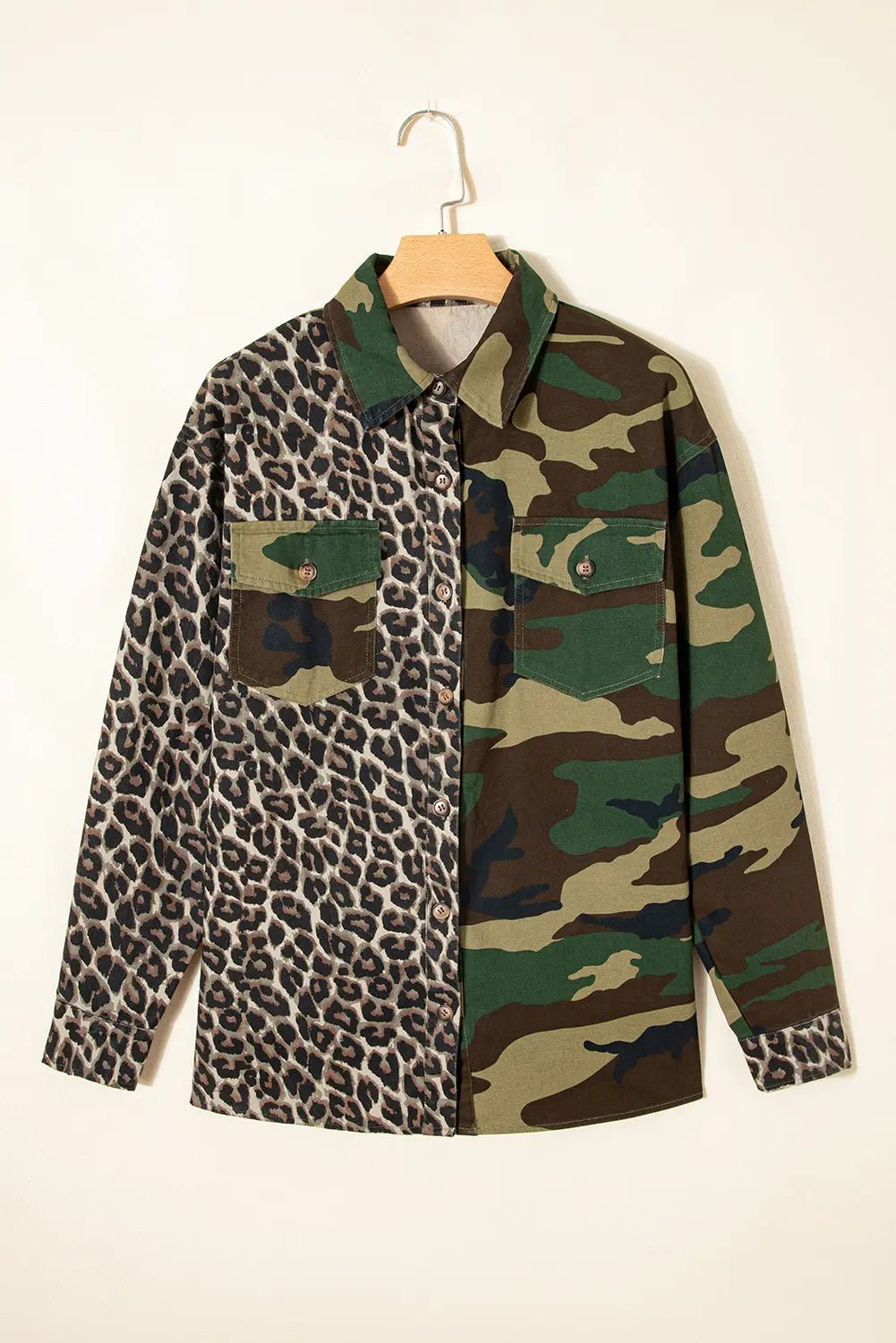 A long-sleeve button-up shirt hanging on a wooden hanger against a plain off-white wall. The shirt features a split design: one half is in a brown, black, and beige leopard print, and the other half is in a green, brown, and beige camouflage pattern.