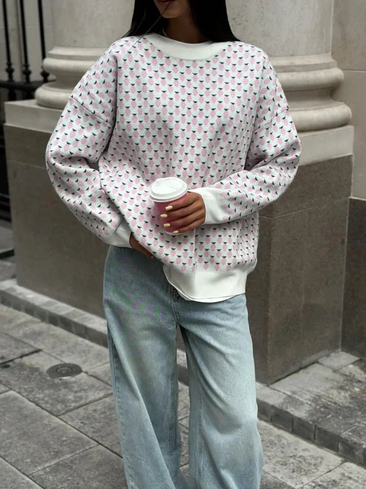 Person wearing a patterned sweater and light blue jeans holding a coffee cup outdoors.