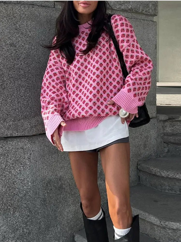 Person wearing a pink patterned sweater and white skirt standing against a stone wall.