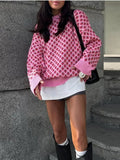 Person wearing a pink patterned sweater and white skirt standing against a stone wall.