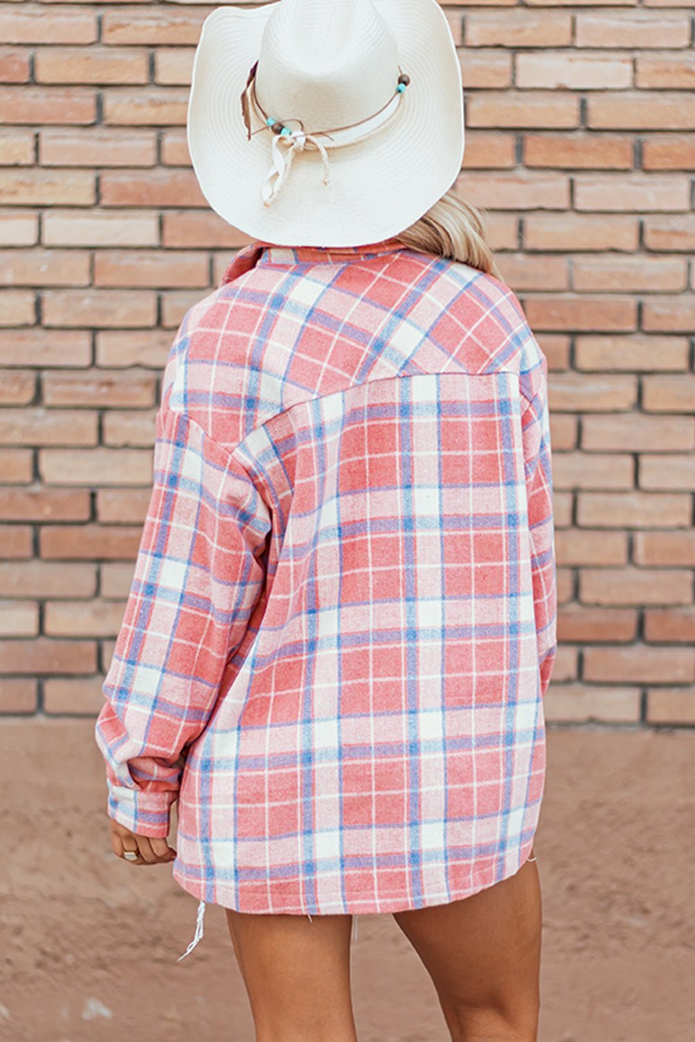 Person wearing a red and white plaid shirt with a white hat against a brick wall.