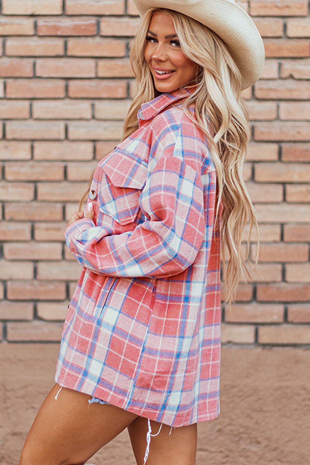 Woman wearing a plaid shirt and cowboy hat against a brick wall.