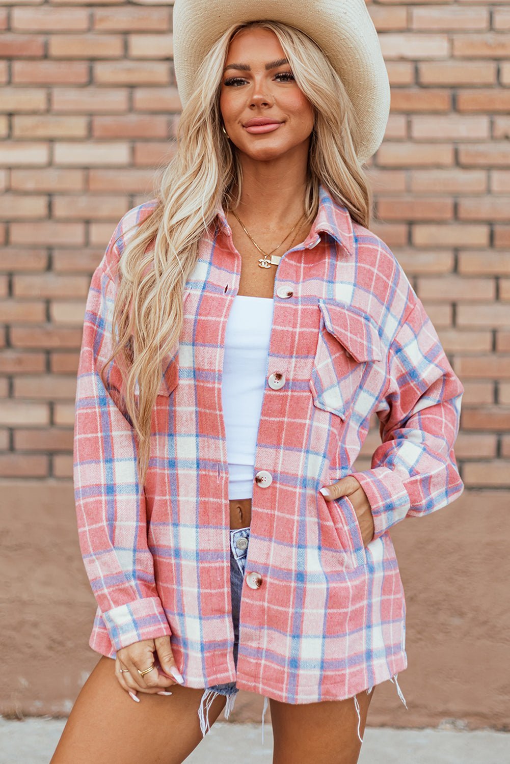 Woman wearing a plaid shirt and cowboy hat against a brick wall.