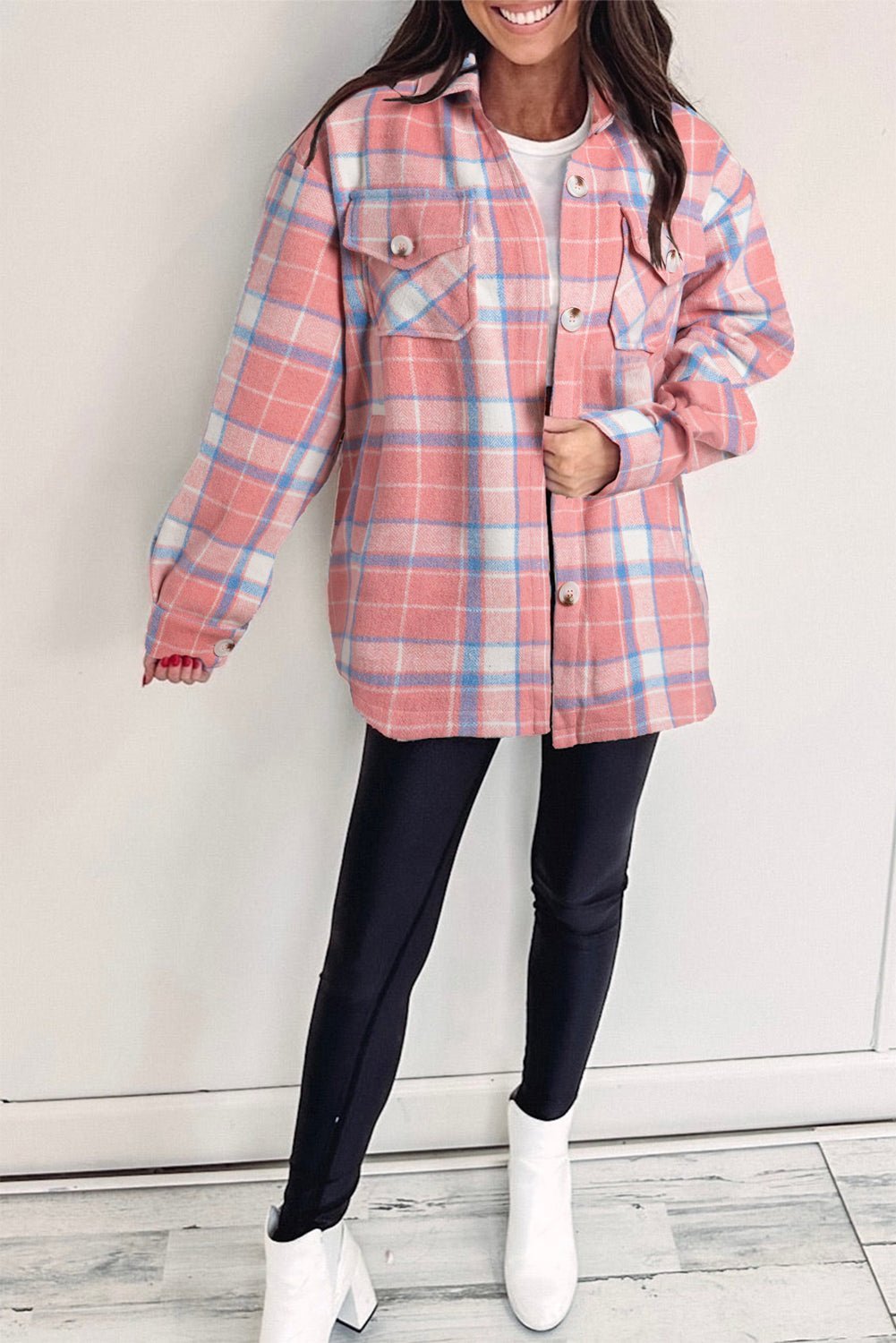 Person wearing a pink and blue plaid jacket with black pants and white shoes on a light background