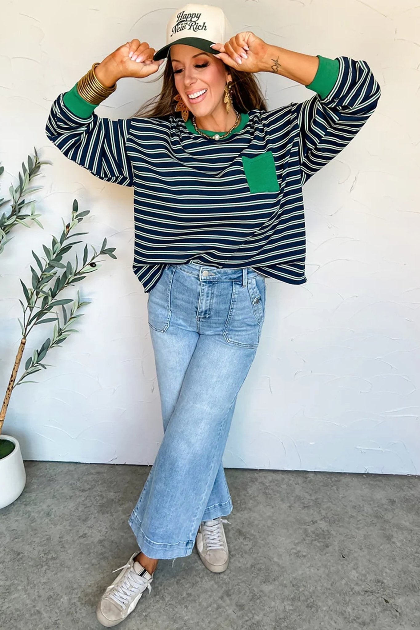 Woman wearing a striped sweater, jeans, and sneakers indoors with a plant in the background