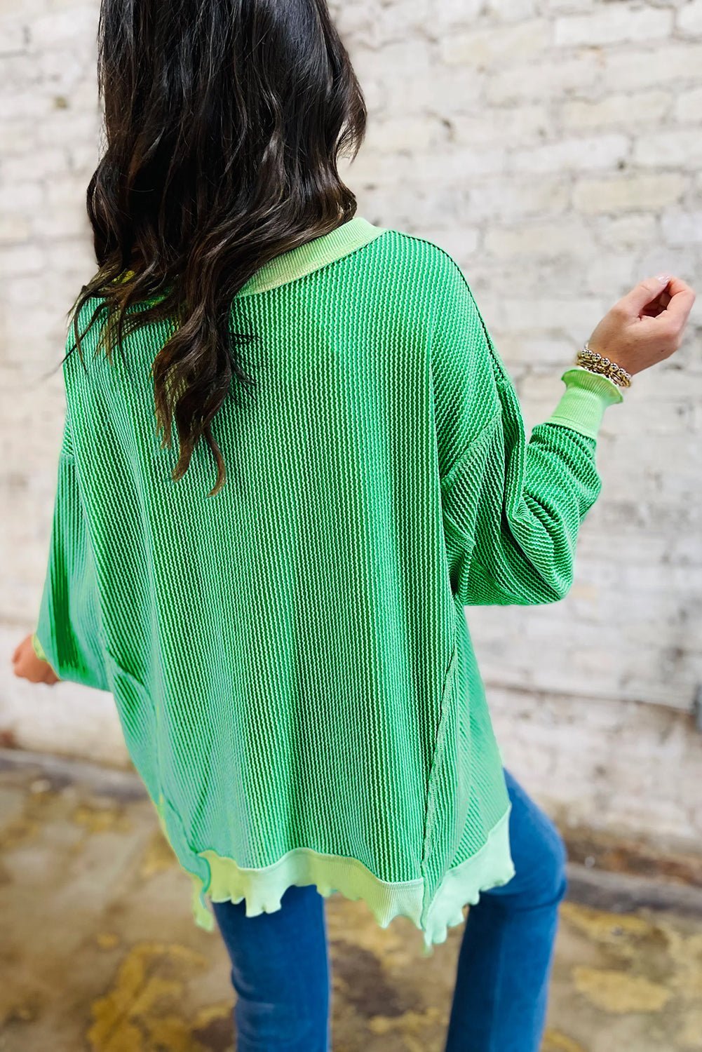 Person wearing a green sweater with a textured pattern against a stone wall background