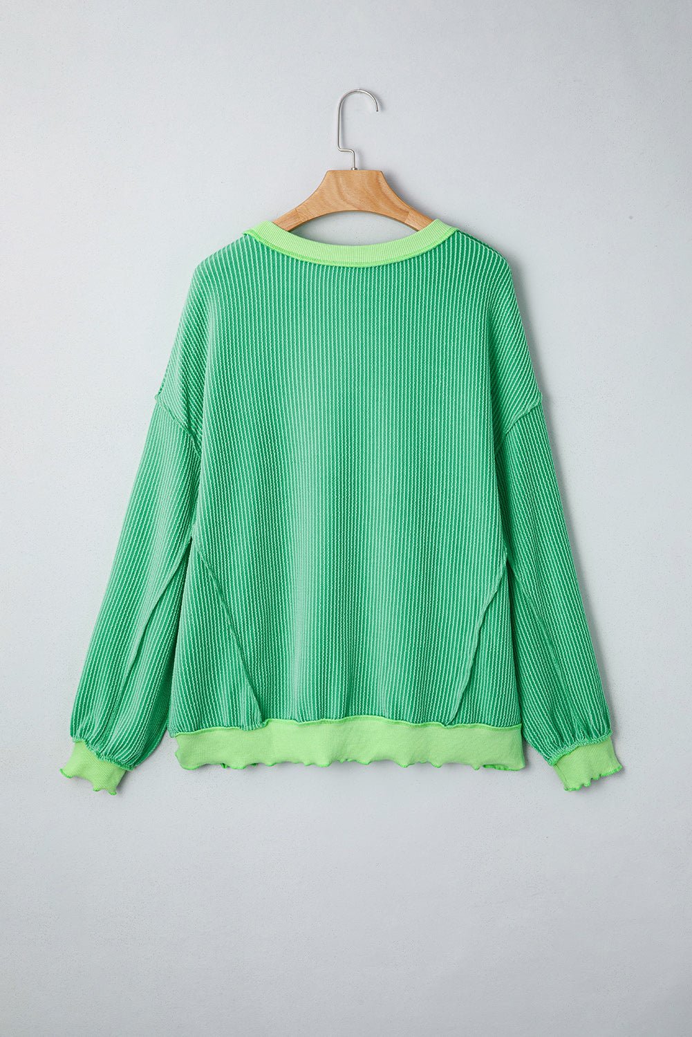 Green ribbed sweater on a wooden hanger against a gray background