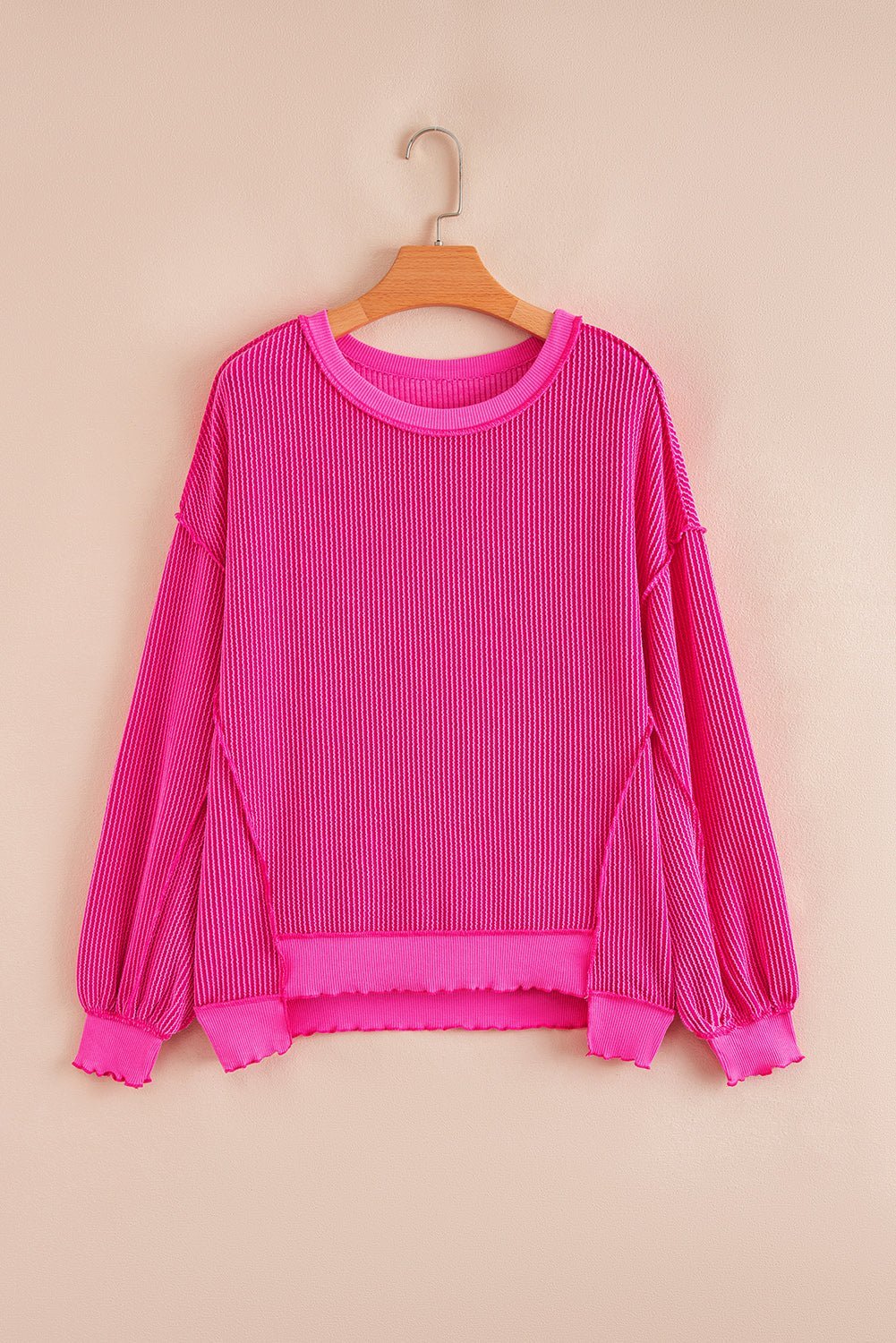 Pink ribbed sweater on a wooden hanger against a beige background