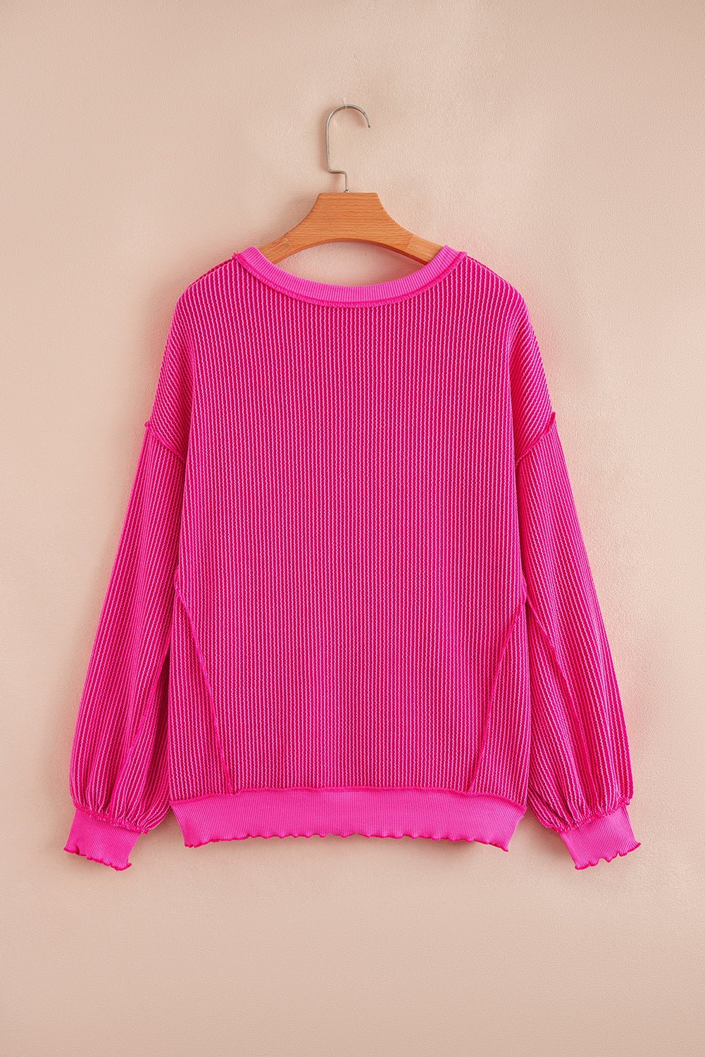 Pink pleated blouse on a hanger against a beige background