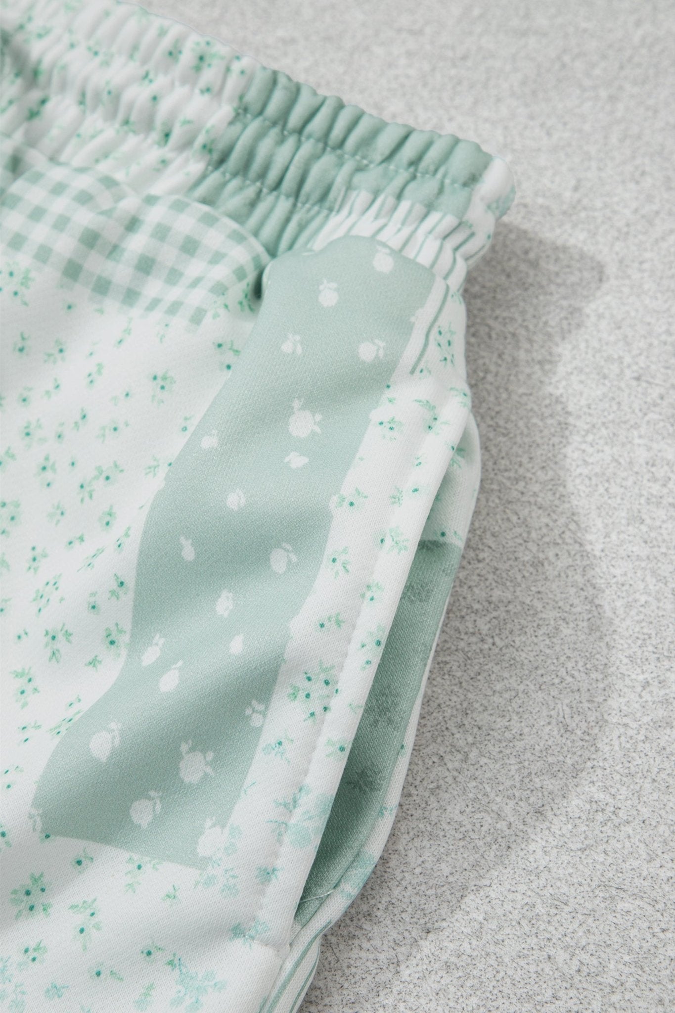 Mint green baby pants with floral, gingham, and solid pocket panels.