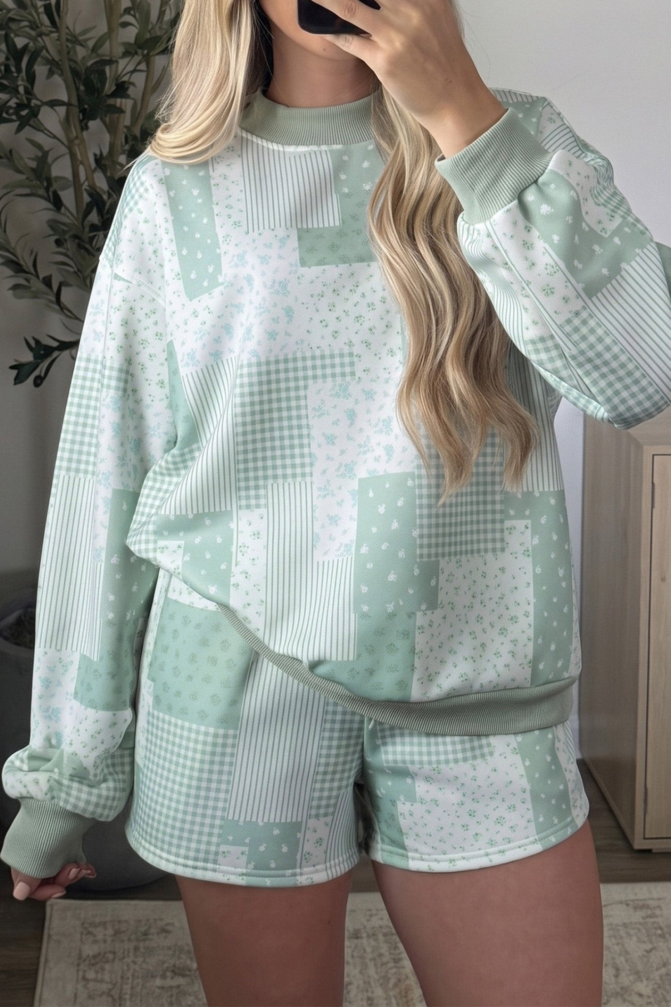 Woman in a sage green and white ditsy floral patchwork sweatshirt and shorts set taking a selfie.