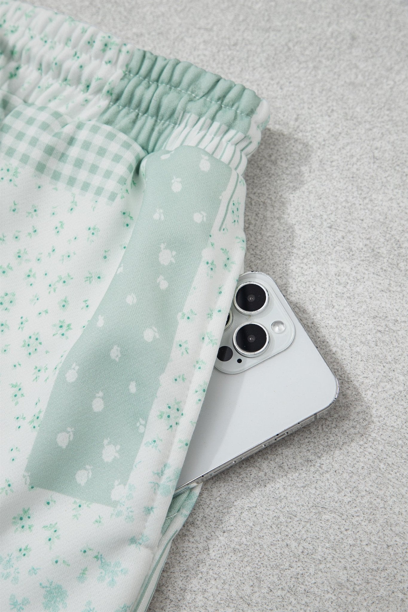 Mint green patterned shorts with gingham waistband beside a white smartphone.