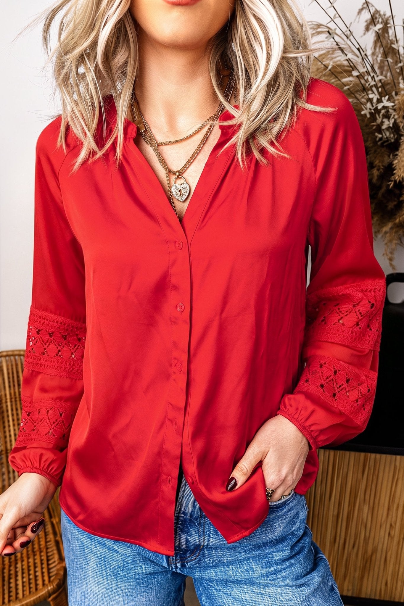 Woman in vibrant red lace-detail button-up blouse with blue jeans.