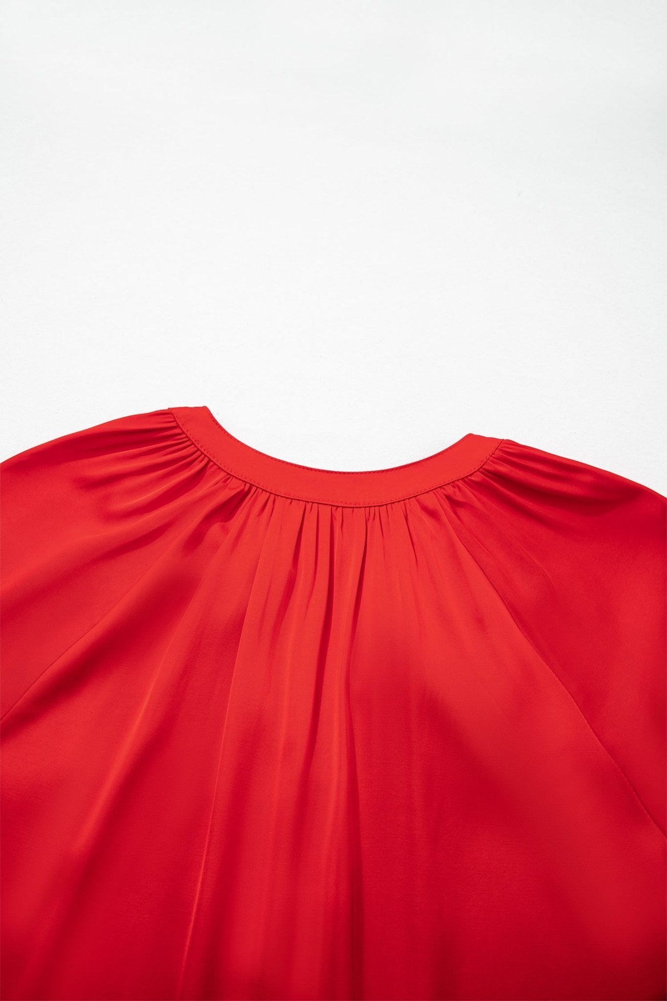 Close-up of bright red blouse with gathered neckline and soft pleated fabric.
