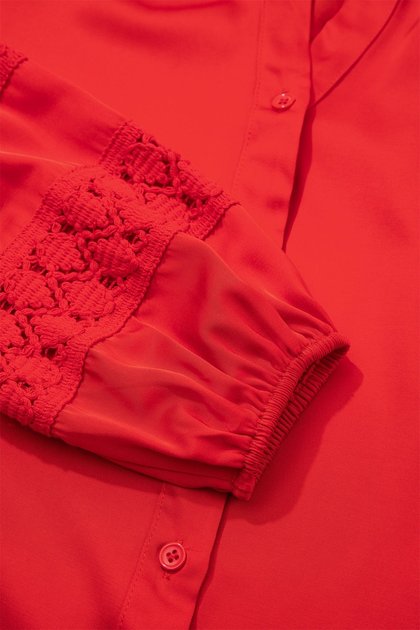 Close-up of bright red blouse with gathered cuff and crochet lace sleeve panel.