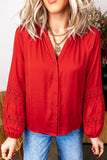 Woman in vibrant red blouse with lace sleeve detailing and blue jeans.