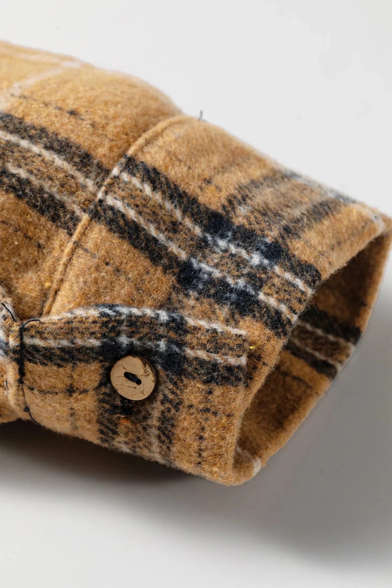 Close-up of a plaid wool or flannel shirt cuff in tan, brown, and black with a visible wooden button.