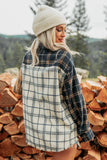Woman in navy-beige-brown plaid flannel and cream beanie by firewood.