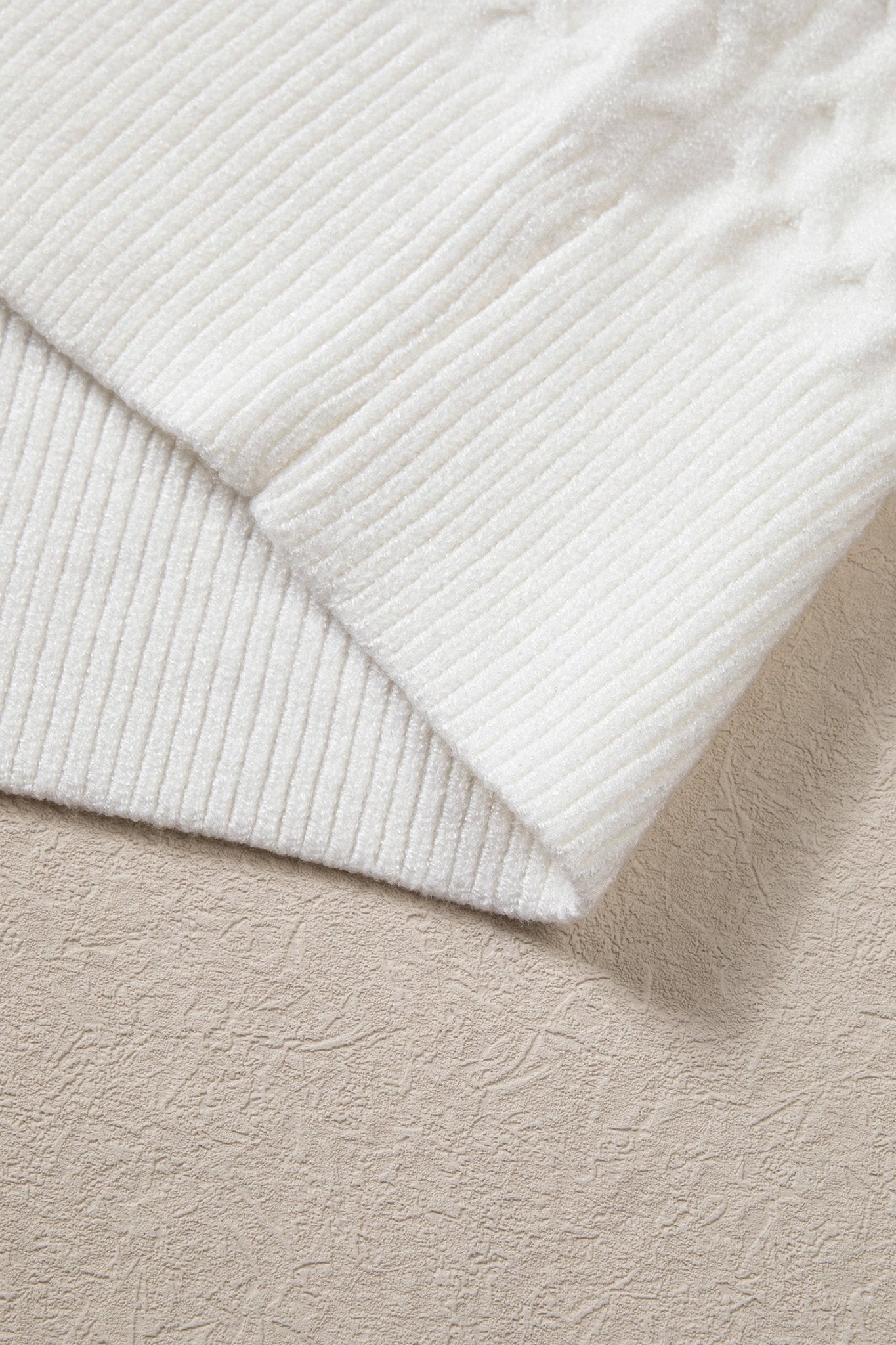 Close-up of folded white ribbed knit fabric with soft corduroy-like ridges on a textured beige surface.