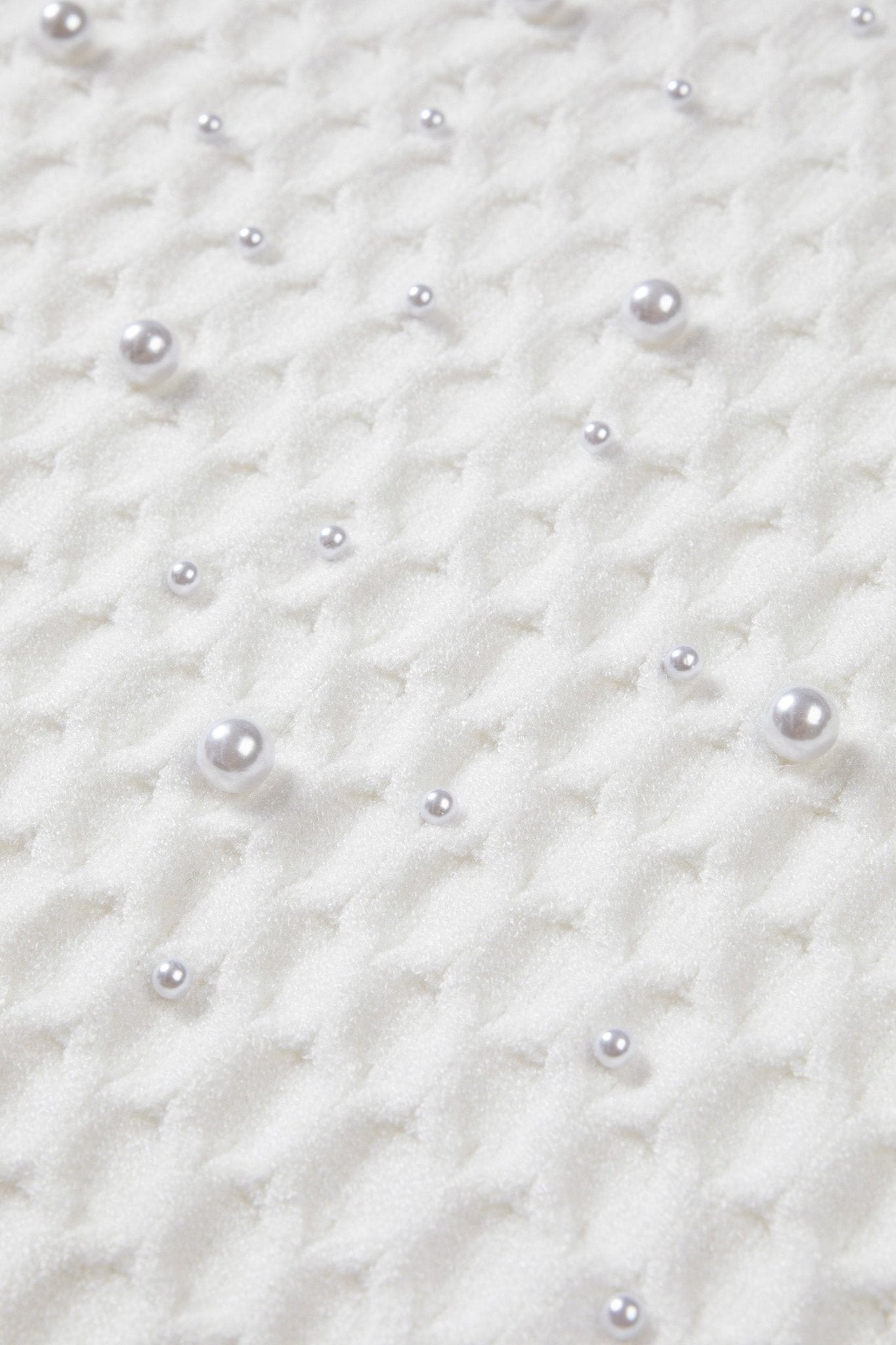 Close-up of a white textured fabric decorated with scattered faux pearl beads in varying sizes.