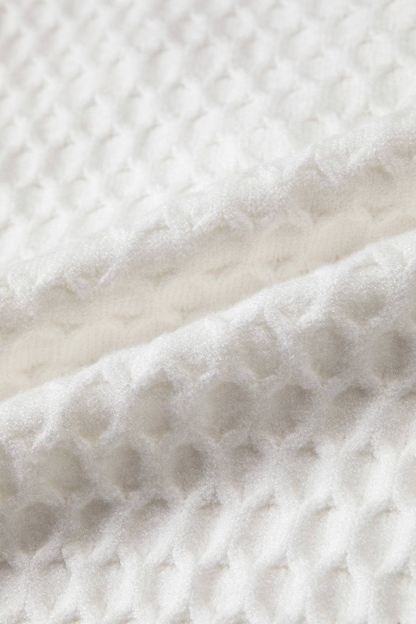 A close-up of a white textured fabric with a waffle or honeycomb-like knit pattern and soft folds.