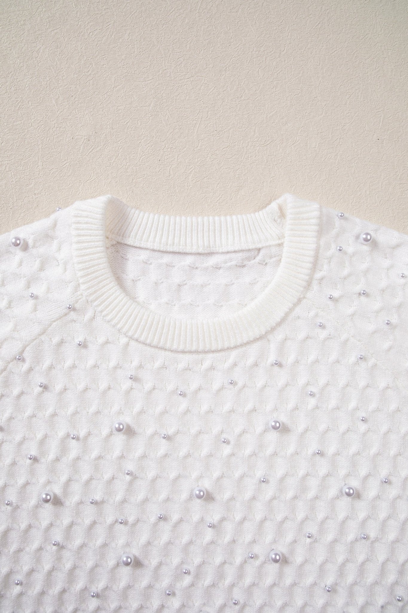 Close-up of white textured knit sweater with silver bead details and ribbed crew neck.