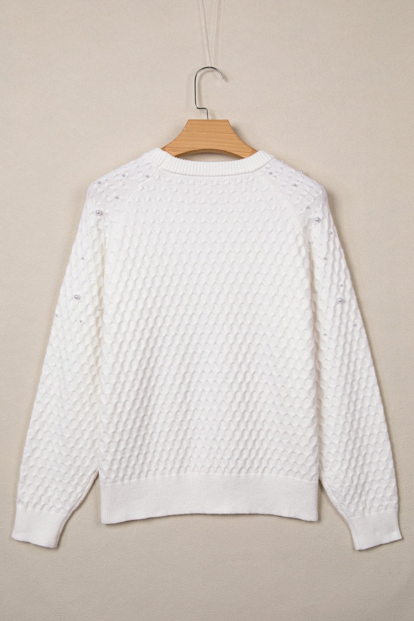 White textured knit sweater with long sleeves, ribbed cuffs and hem, hanging on a wooden hanger.