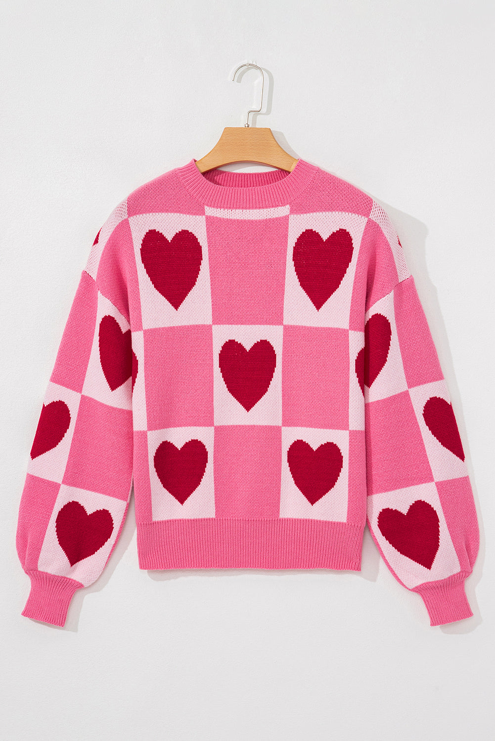 Pink heart checkered crew neck sweater with ribbed cuffs on a hanger, front view